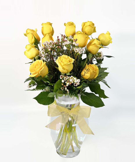 Bright yellow roses with seeded eucalyptus in a clear glass vase. 
