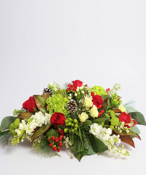 Christmas centerpiece of winter greenery, red roses, pine cones, gold accents, and red taper candles. 