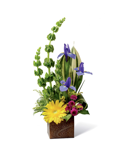 Gerbera daisies, Bells of Ireland, iris, tropical greenery, solidago, button poms and more in a rustic square woodern planter.