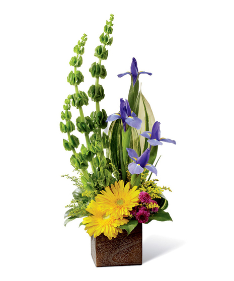 Gerbera daisies, Bells of Ireland, iris, tropical greenery, solidago, button poms and more in a rustic square woodern planter.