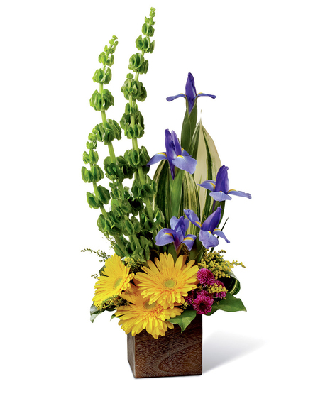 Gerbera daisies, Bells of Ireland, iris, tropical greenery, solidago, button poms and more in a rustic square woodern planter.