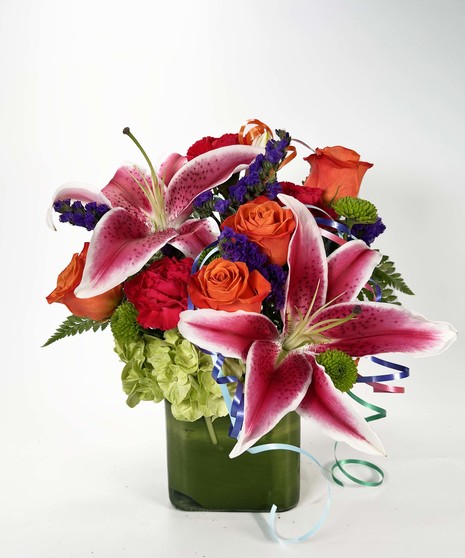 Orange, purple, pink and green flowers in a leaf-lined cube vase.