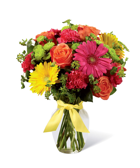 Hot pink, orange and yellow flowers in a clear glass vase tied with yellow ribbon.