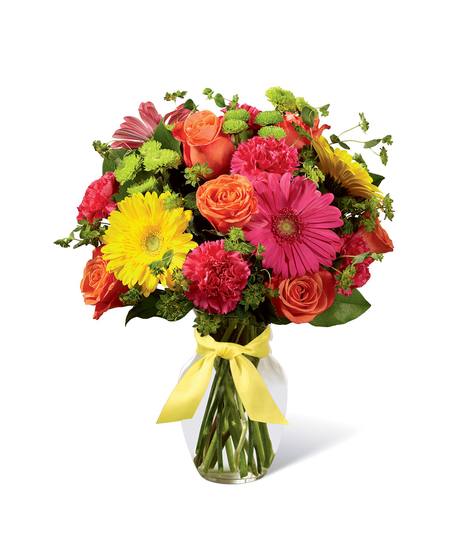 Hot pink, orange and yellow flowers in a clear glass vase tied with yellow ribbon.
