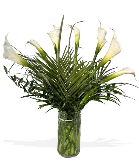 Bouquet of white calla lilies in a clear glass vase with greenery.