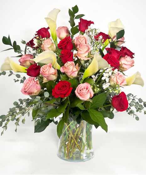 Long stemmed red and pink roeses and white calla lilies in a clear glass vase.