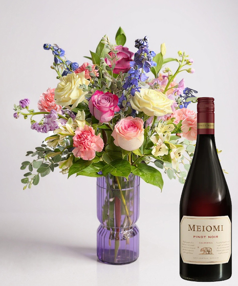 Red cube vase filled with roses in red, pink and lavender with greenery.