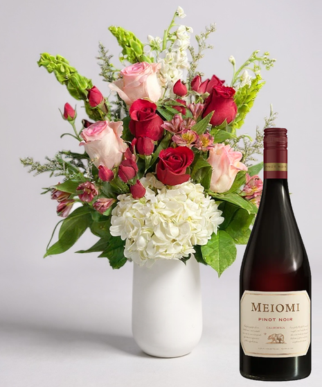 Red cube vase filled with roses in red, pink and lavender with greenery.