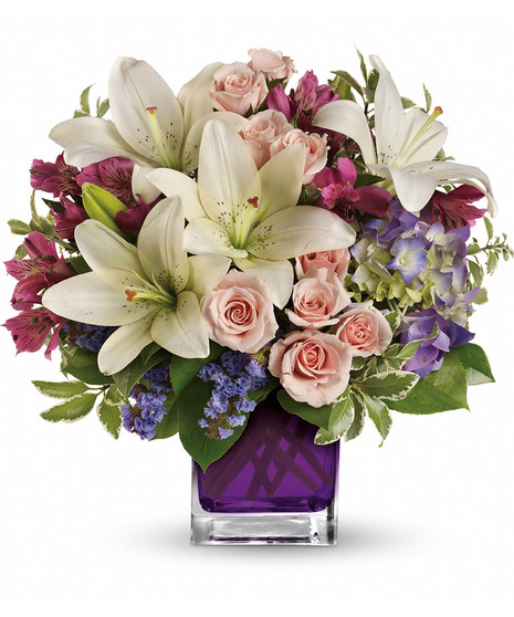 PUrple hydrangea, light pink spray roses, and white asiatic lilies in a violet glass cube vase. 