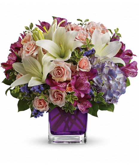 PUrple hydrangea, light pink spray roses, and white asiatic lilies in a violet glass cube vase. 