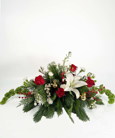 Holiday centerpiece of red roses, berries, greenery, and more accented with a red ribbon and red taper candles. 
