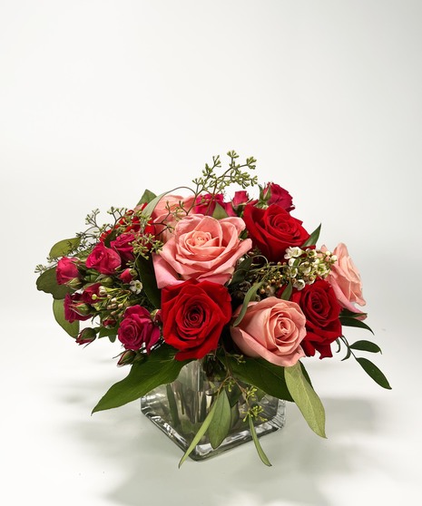 Red cube vase filled with roses in red, pink and lavender with greenery.