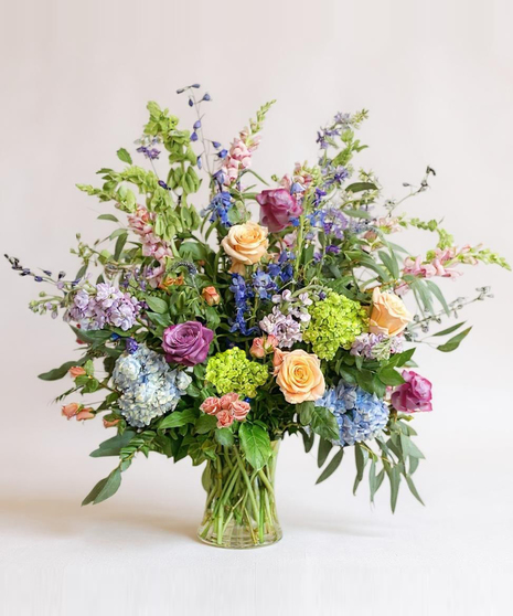 Sympathy wreath of pastel pink, peach and purple flowers with coordinating ribbon. 