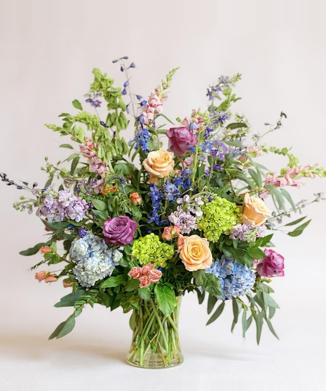 Sympathy wreath of pastel pink, peach and purple flowers with coordinating ribbon. 