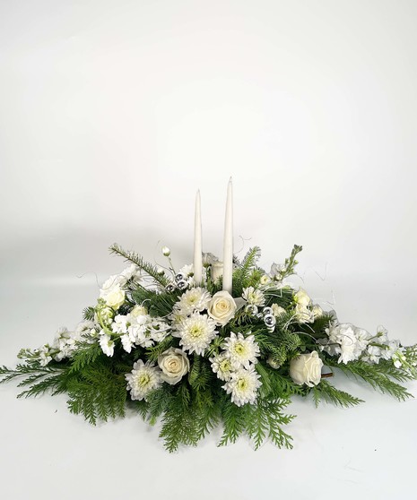 Christmas centerpiece of red flowers, winter greenery, gold ribbon and red taper candles. 