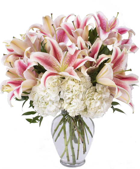 Clear glass vase filled with stargazer lilies and greenery. 