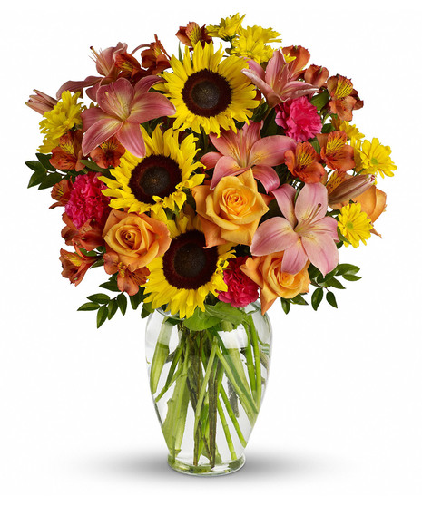 Sunflowers, orange roses and pink lilies in a clear glass vase. 