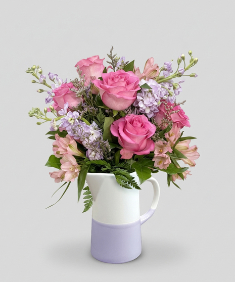 Red cube vase filled with roses in red, pink and lavender with greenery.