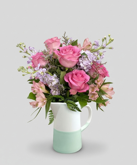 Red cube vase filled with roses in red, pink and lavender with greenery.