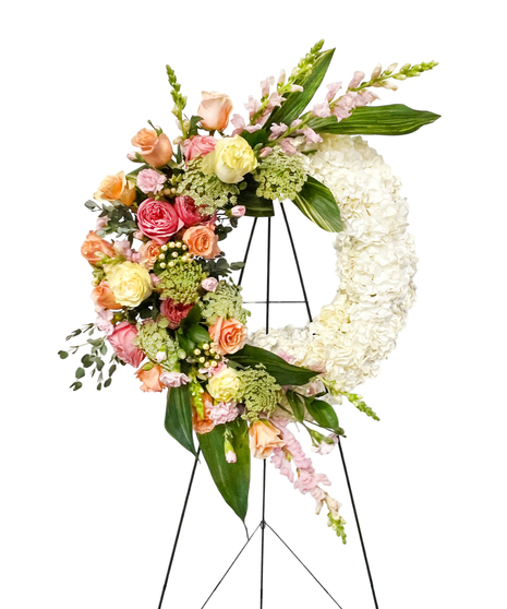 Sympathy wreath of pastel pink, peach and purple flowers with coordinating ribbon. 