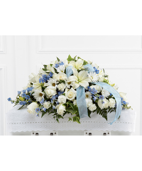 Casket spray of white roses, daisies, and more with blue delphinium and blue ribbon. 