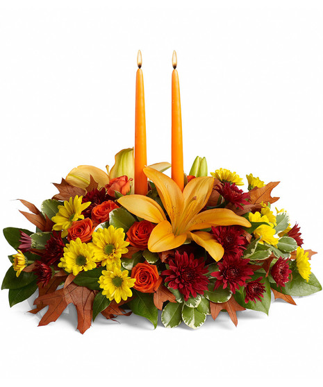 Fall centerpiece featuring orange roses, Asiatic lilies, and more with taper candles.