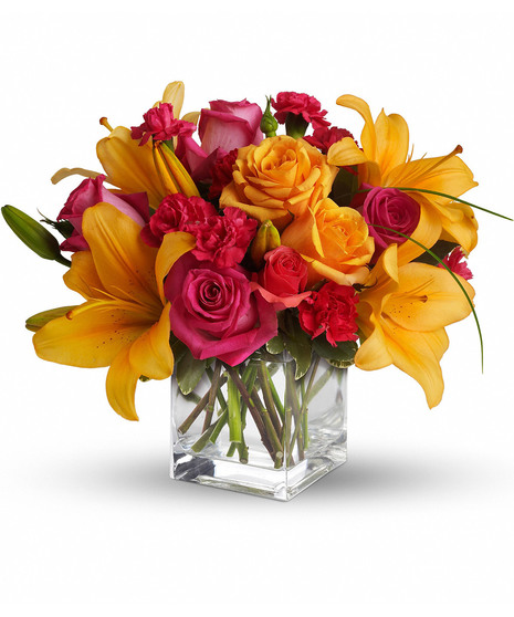Bright hot pink and orange flowers in a clear glass cube vase.