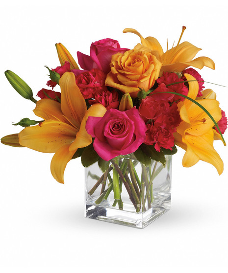 Bright hot pink and orange flowers in a clear glass cube vase.
