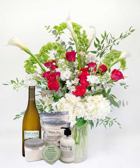 Long stemmed red and pink roeses and white calla lilies in a clear glass vase.