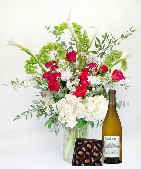 Long stemmed red and pink roeses and white calla lilies in a clear glass vase.
