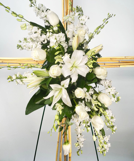Sympathy cross of river cane and floral accents presented on an easel. 