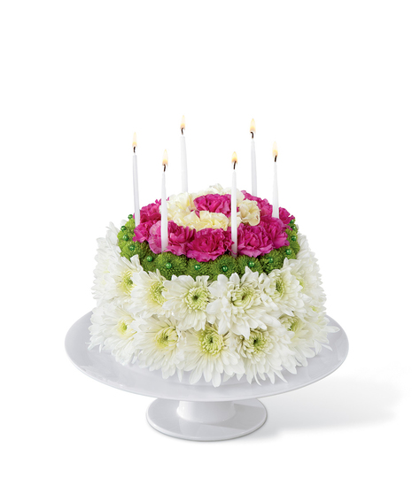 Cake made entirely of flowers on a white cake plate with candles.