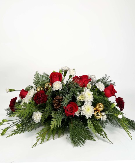 Christmas centerpiece of winter greenery, red roses, pine cones, gold accents, and red taper candles. 