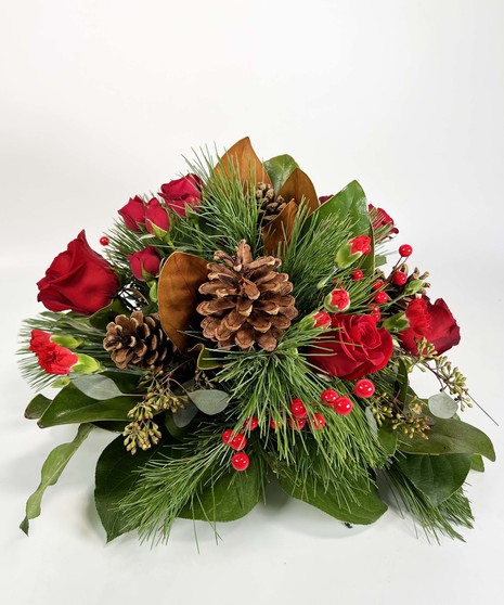 Holiday centerpiece of greenery, red roses, pine cones, berries and a red center candle. 