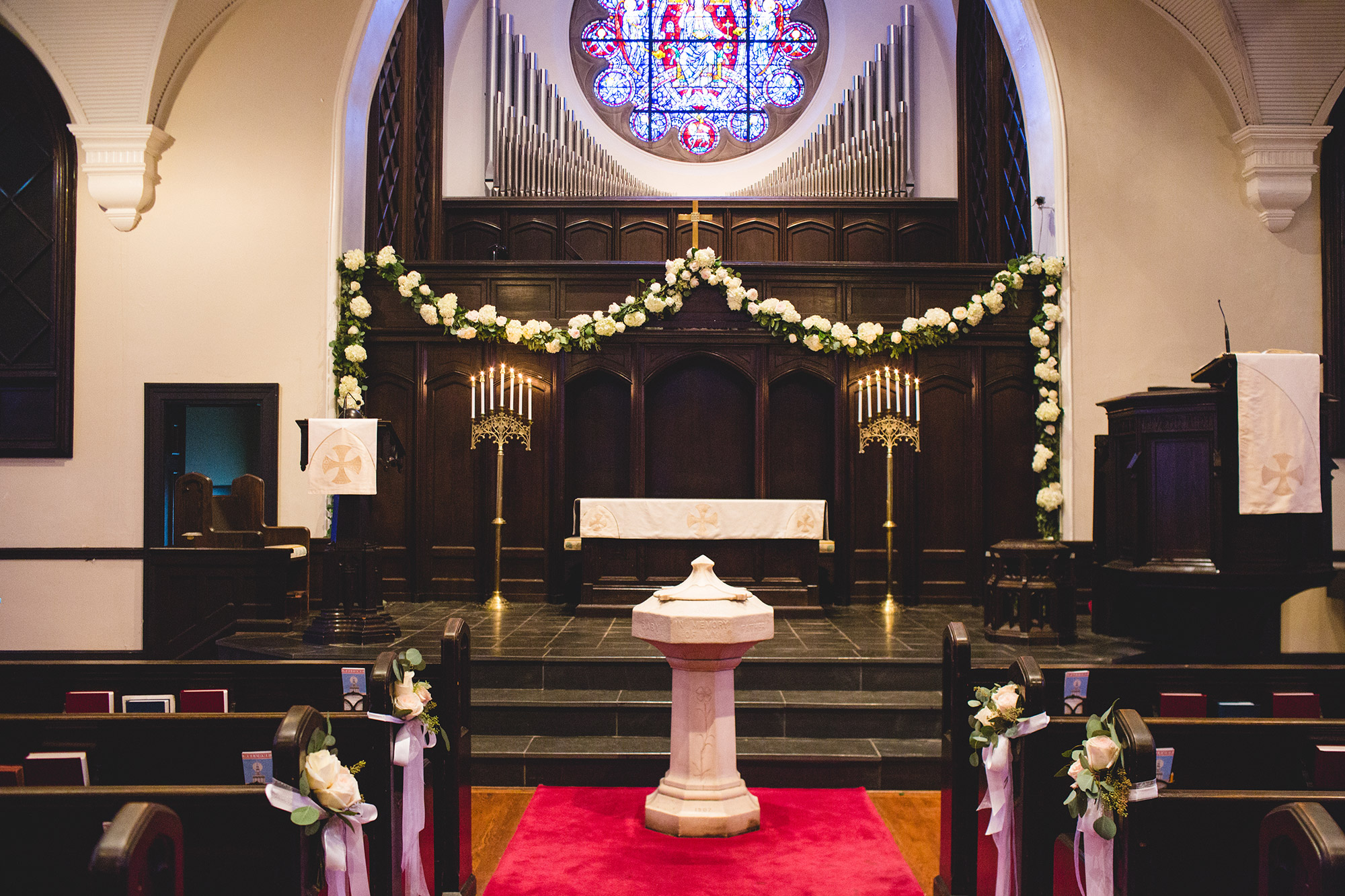 Gorgeous white flowers are draped behind the altar before a wedding, while smaller bouquets adorn two rows of pews